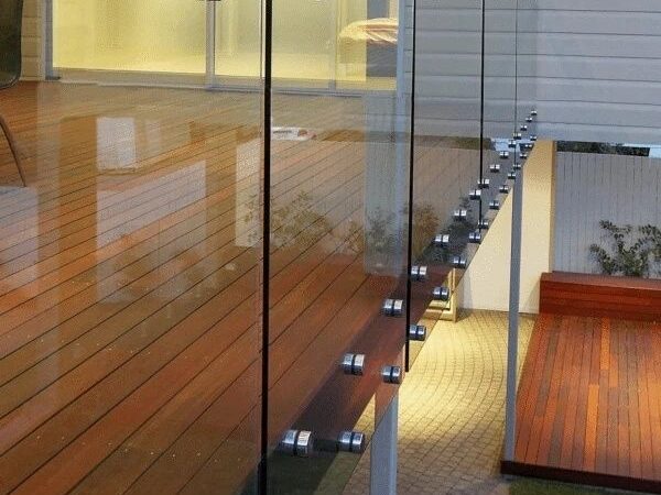 Glazen balustrade met zichtbare puntbevestigingen langs een houten terras