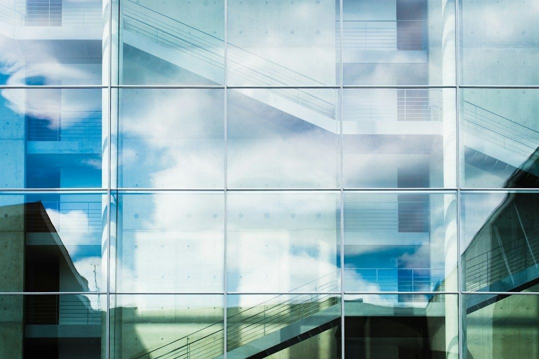 Grote glazen gevel met weerspiegelde wolken en zichtbare gebouwstructuur